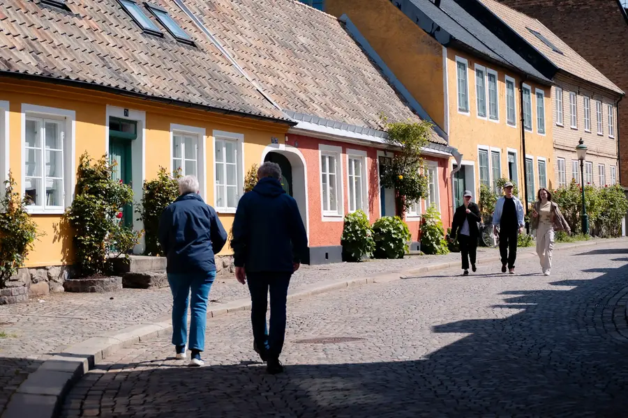 Två sällskap går längs en av Lunds gamla gator. Gamla gathus i glada färger kantar gatan.